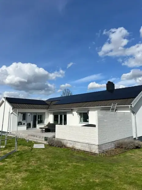 Vitt enplanshus med solpaneler på taket, sett från trädgården.