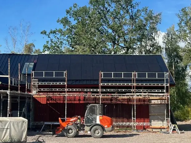 Ekonomibyggnad med byggnadsställning längs fasaden under pågående takarbete.