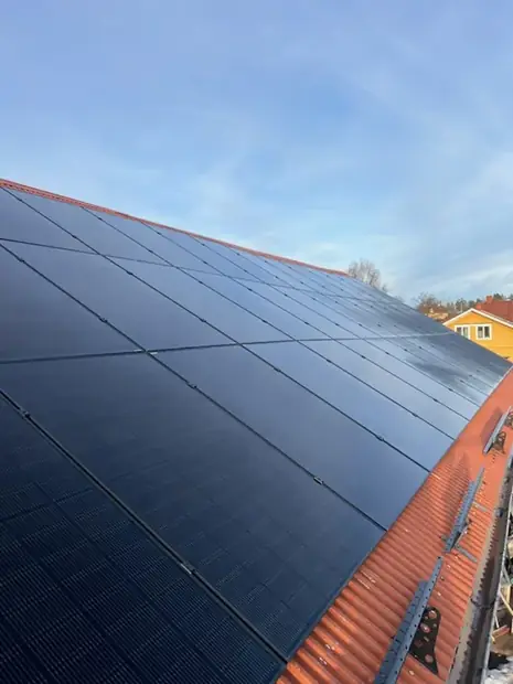 Svarta solpaneler monterade på ett rött tegeltak på en villa.