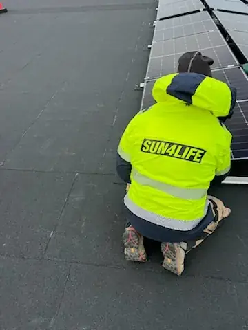 Montör i gul varselväst med Sun4Life-tryck som arbetar med panelrader på ett tak.