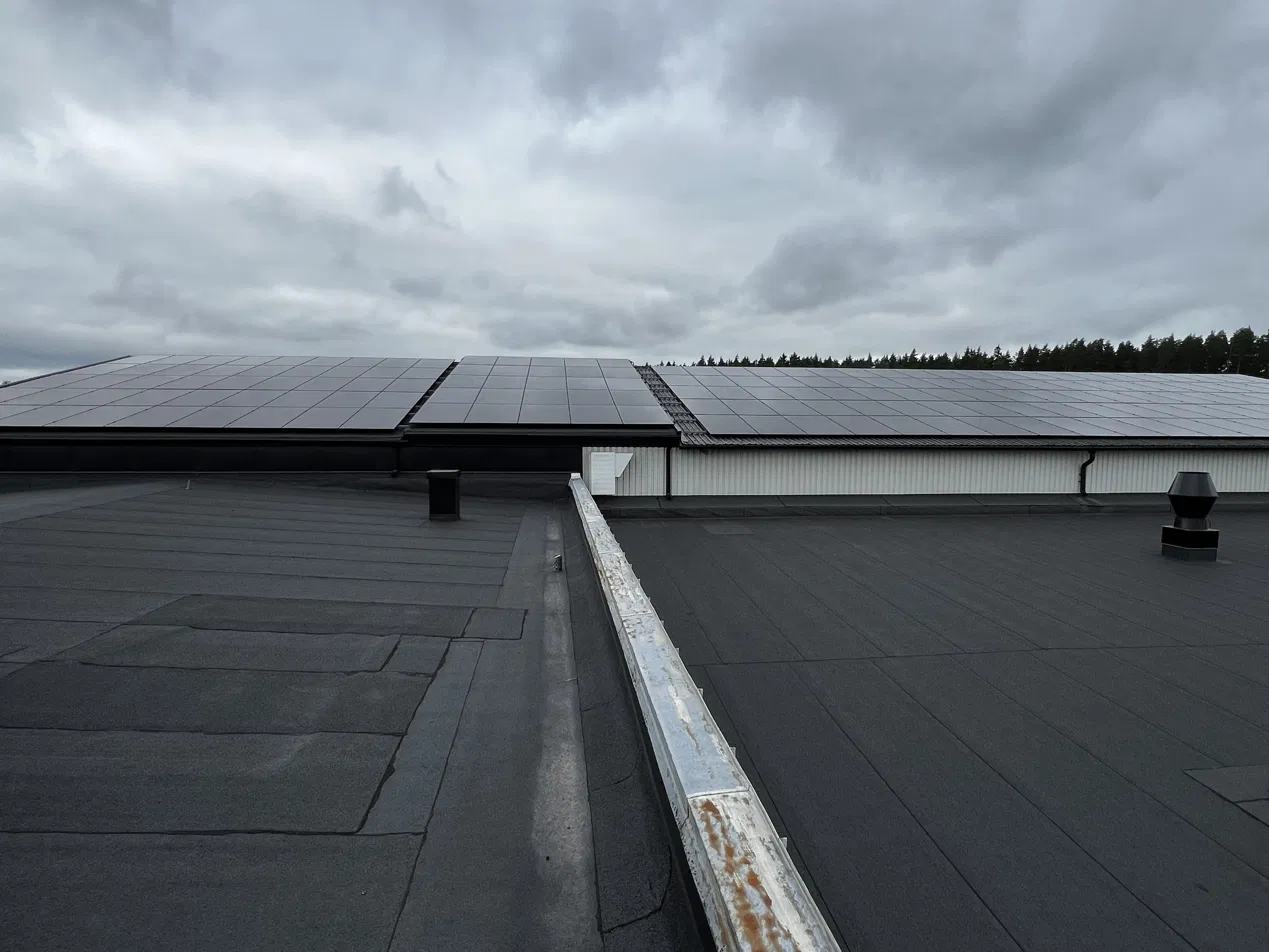 Översiktsbild över ett platt industritak täckt av solpaneler under mulen himmel.
