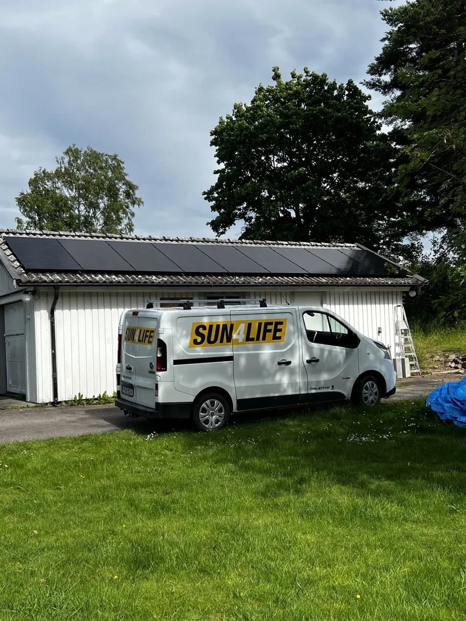 Sun4Lifes servicebil parkerad framför ett garage med solpaneler på taket.