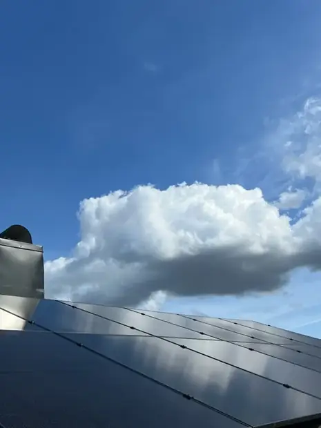 Solpaneler sedda underifrån mot en blå himmel med lätta moln.