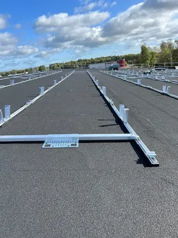 Monteringsskenor utlagda på ett svart papptak inför panelmontage.