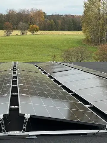 Solpanelrad på ett tak med åkerlandskap i bakgrunden.