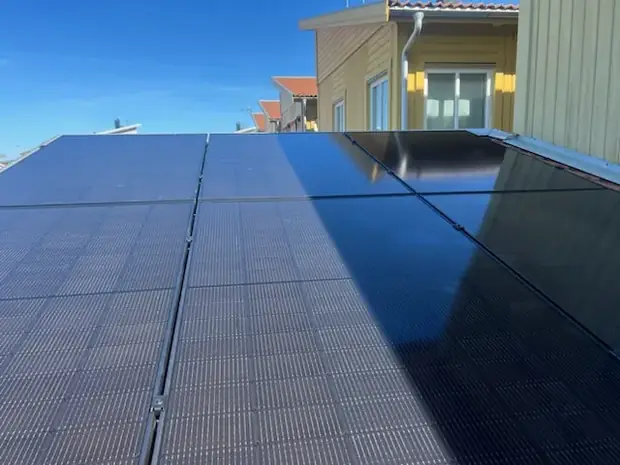 Helsvarta solpaneler på ett tak med en byggnad i bakgrunden.