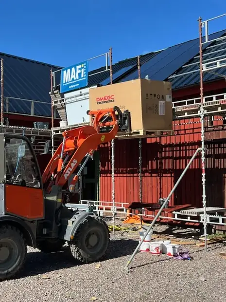 Kranbil som lyfter material till taket på en ekonomibyggnad under montage.